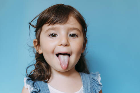 Portrait of cute little girl with tongue out on blue background - GEMF03189