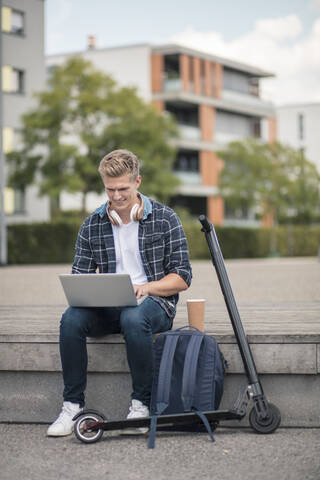 Young businessman with e-scooter using laptop in the city stock photo