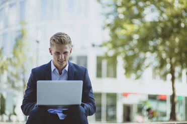 Young businessman using laptop in the city - MOEF02483