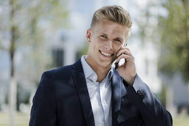 Porträt eines lächelnden jungen Geschäftsmannes, der mit einem Handy telefoniert - MOEF02488