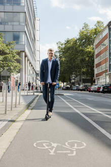 Junger Geschäftsmann fährt E-Roller auf dem Fahrradweg in der Stadt - MOEF02505