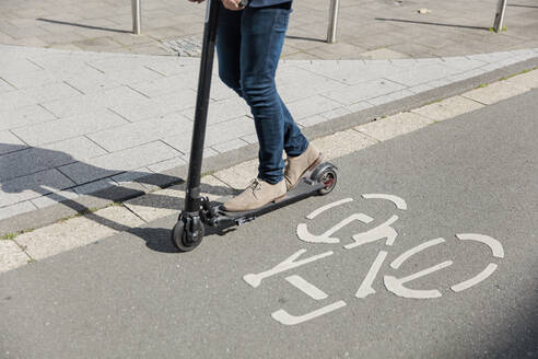 Beine eines Mannes, der einen E-Scooter auf dem Fahrradweg in der Stadt fährt - MOEF02506