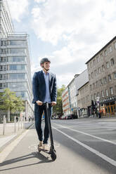 Junger Geschäftsmann fährt E-Roller auf dem Fahrradweg in der Stadt - MOEF02508