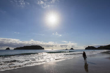 New Zealand, North Island, Waikato, Sun shining over silhouette of woman standing alone on Hahei Beach - FOF10964