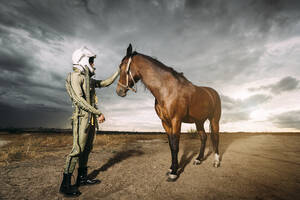 Mann als Astronaut gekleidet mit einem Pferd auf einer Wiese mit dramatischen Wolken im Hintergrund - DAMF00087