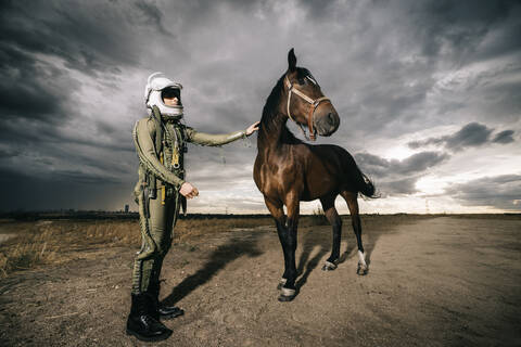 Mann als Astronaut gekleidet mit einem Pferd auf einer Wiese mit dramatischen Wolken im Hintergrund, lizenzfreies Stockfoto