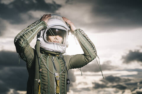 Mann posiert als Astronaut gekleidet mit dramatischen Wolken im Hintergrund, lizenzfreies Stockfoto