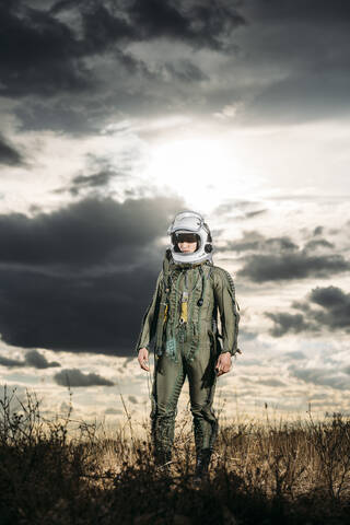 Mann posiert als Astronaut verkleidet auf einer Wiese mit dramatischen Wolken im Hintergrund, lizenzfreies Stockfoto