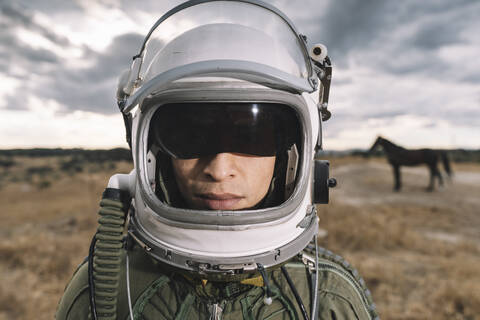 Mann posiert als Astronaut verkleidet auf einer Wiese mit dramatischen Wolken im Hintergrund, lizenzfreies Stockfoto