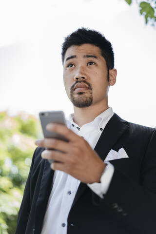 Junger Geschäftsmann hält Mobiltelefon im Freien, lizenzfreies Stockfoto