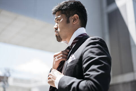 Young businessman in the city adjusting his tie stock photo