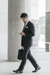 Young businessman with cell phone walking in the city - JPIF00188