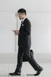 Young businessman with cell phone walking in the city - JPIF00189