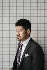 Portrait of young businessman at tiled wall - JPIF00197