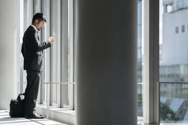 Junger Geschäftsmann benutzt Handy am Fenster - JPIF00198