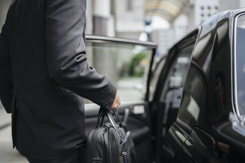 Mittelteil eines Geschäftsmannes beim Einsteigen in ein Taxi - JPIF00209