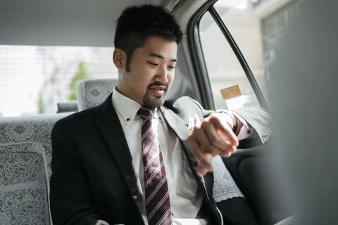 Young businessman in a taxi checking the time stock photo