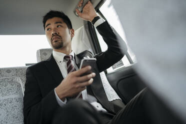 Junger Geschäftsmann mit Mobiltelefon in einem Taxi - JPIF00215