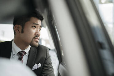 Junger Geschäftsmann in einem Taxi schaut aus dem Fenster - JPIF00217