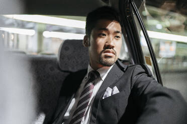 Junger Geschäftsmann in einem Taxi schaut aus dem Fenster - JPIF00223