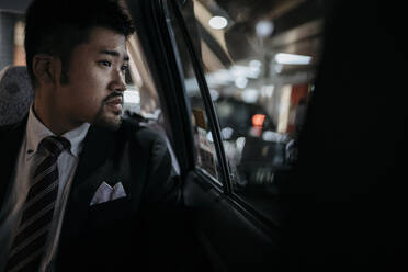 Junger Geschäftsmann in einem Taxi schaut aus dem Fenster - JPIF00225