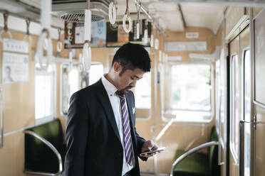 Young businessman using cell phone on a train - JPIF00230