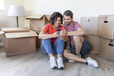 Happy couple using cell phone in new home - WPEF01923