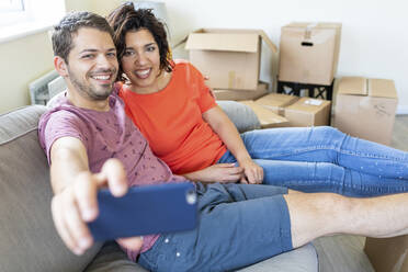 Happy couple taking a selfie on couch in new home - WPEF01934