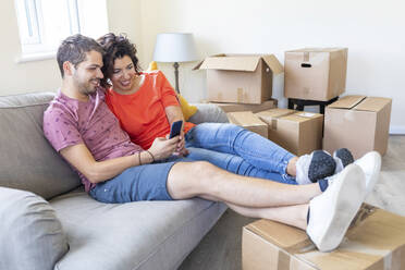 Happy couple using cell phone on couch in new home - WPEF01935