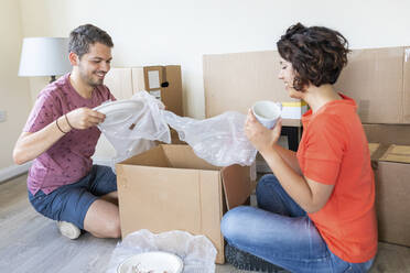 Happy couple moving into new home unpacking cardboard box - WPEF01937