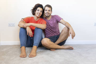 Portrait of happy couple sitting on the floor in new home - WPEF01955