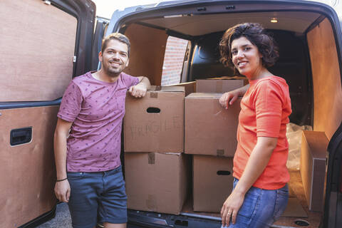 Porträt eines lächelnden Paares an einem Lieferwagen mit Pappkartons, lizenzfreies Stockfoto