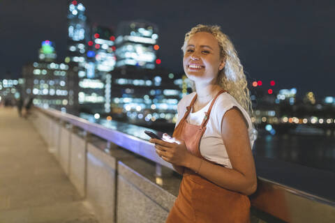 Junge Frau in London bei Nacht, die ihr Smartphone benutzt, lizenzfreies Stockfoto