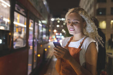 Junge Frau in London bei Nacht, die auf ihr Smartphone schaut, Bus im Hintergrund - WPEF01991