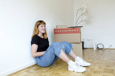 Smiling young student sitting on the floor during move - FLLF00306