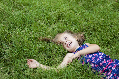 Lachendes kleines Mädchen auf einer Sommerwiese liegend, lizenzfreies Stockfoto