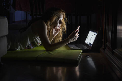 Young woman using laptop and cell phone late at night stock photo