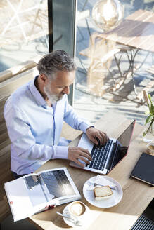 Älterer Mann mit Laptop in einem Café mit Buch auf dem Tisch - FKF03639