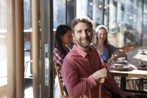 Portrait of smiling man with friends in a cafe - FKF03646