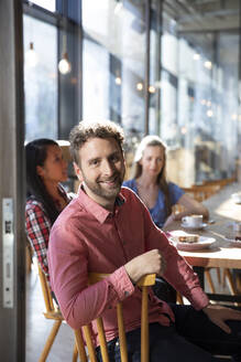 Portrait of smiling man with friends in a cafe - FKF03647