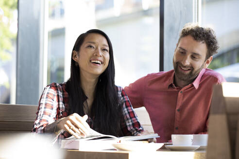 Happy man and woman with book in a cafe - FKF03651