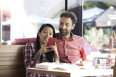 Happy man and woman with cell phone and earbuds in a cafe - FKF03652