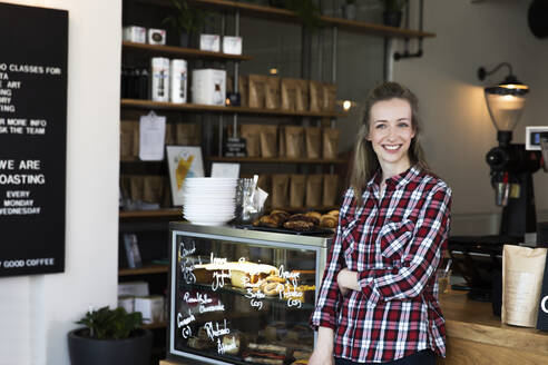 Portrait of smiling woman at the counter of a cafe - FKF03656