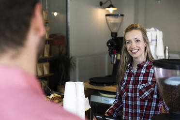 Lächelnde Frau am Tresen eines Cafés, die einen Mann ansieht - FKF03657