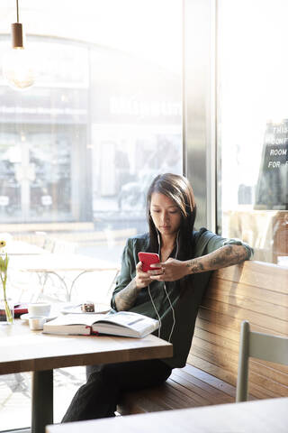 Frau mit Ohrstöpseln und Mobiltelefon in einem Café, lizenzfreies Stockfoto