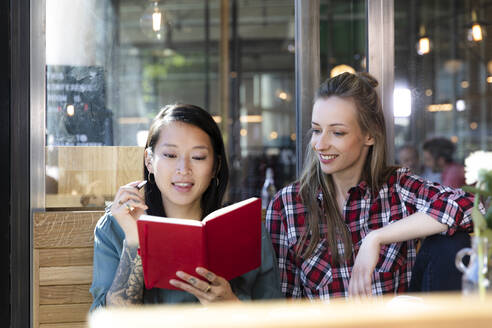 Two women with book in a cafe - FKF03661