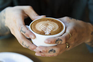 Tätowierte Hände halten eine Tasse Cappuchino - FKF03663