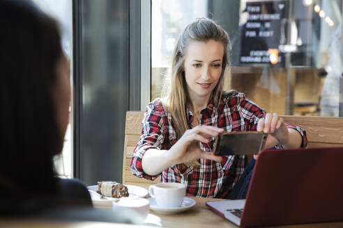 Woman using cell phone and laptop in a cafe - FKF03665