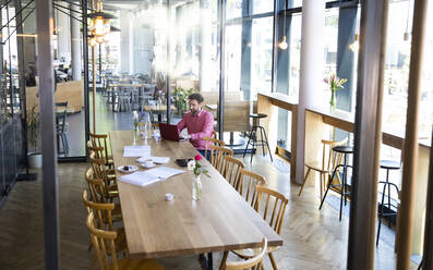 Young man using laptop at wooden table in a cafe - FKF03668