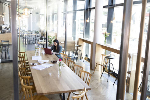 Woman using laptop at wooden table in a cafe - FKF03669